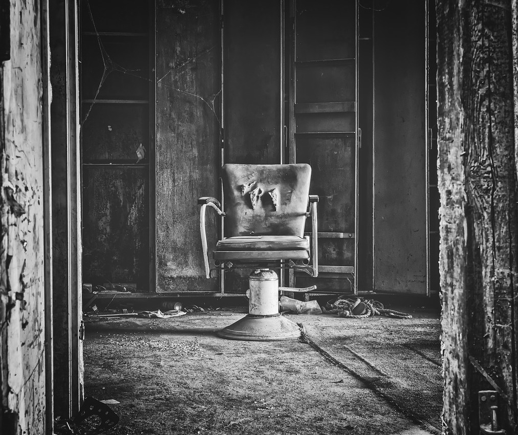 Image Description: Black and white photograph of an old, torn chair sitting in an empty room.